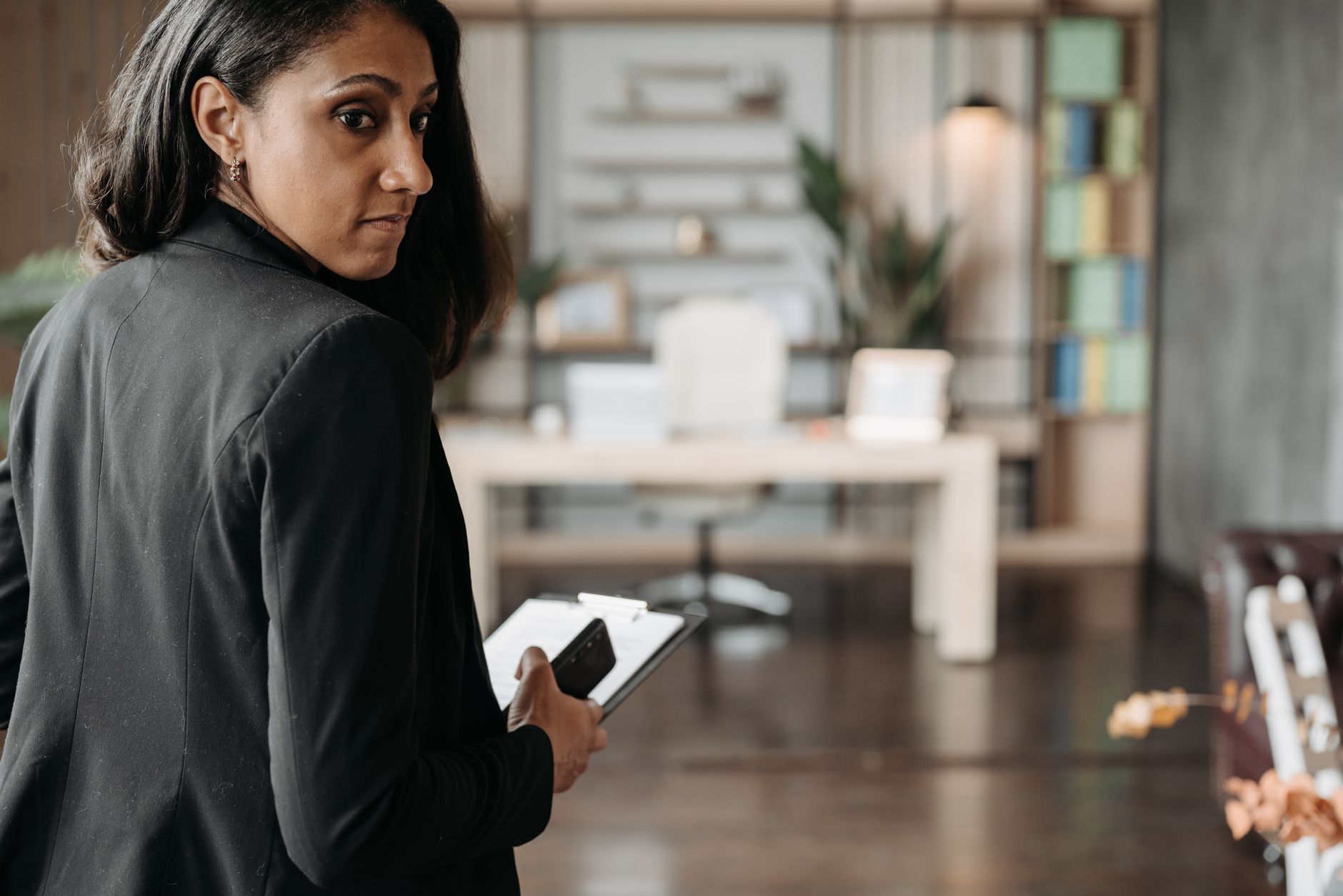 Confident businesswoman in a black suit holding a phone in a chic office interior.