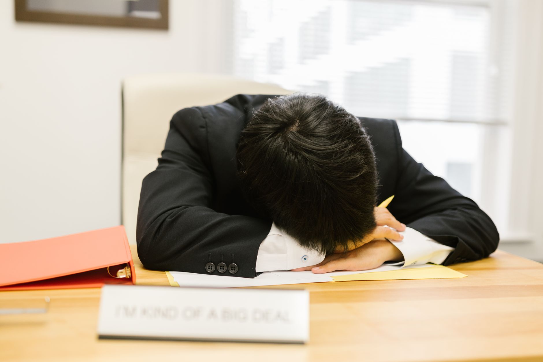 Business person asleep on a desk in an office, illustrating workplace fatigue.