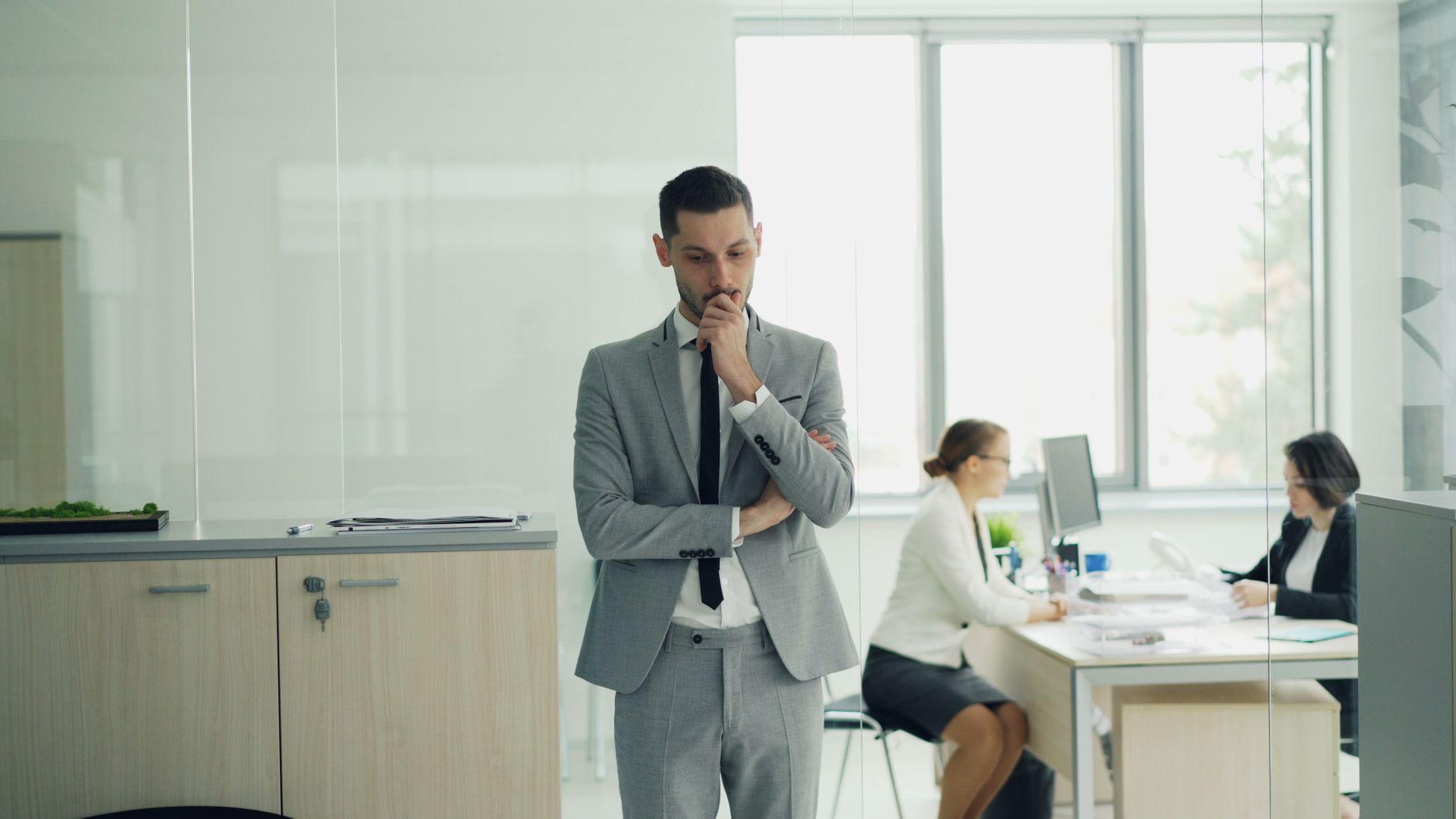 Thoughtful businessman in a modern office setting with colleagues working in the background.