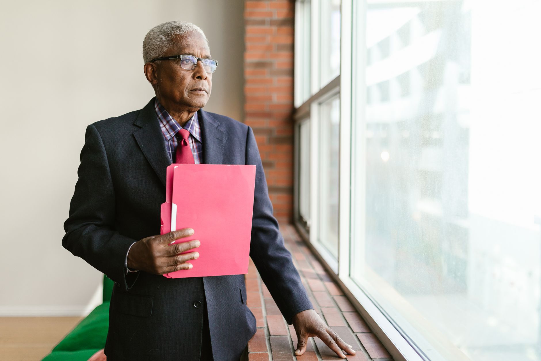 Mature man in suit and glasses holding a folder, gazing out the window.