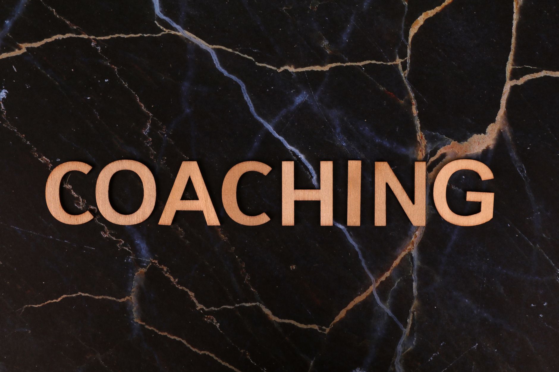 Wooden letters spelling 'Coaching' on dark marble surface, emphasizing guidance and mentorship.