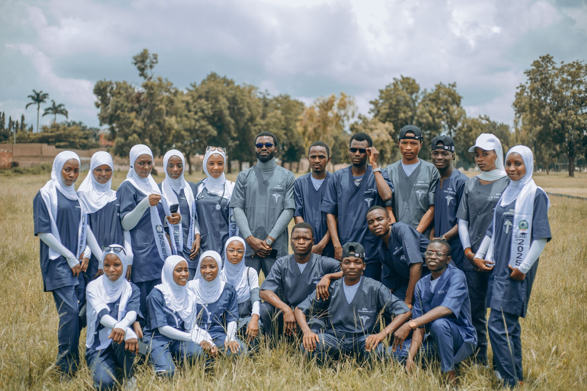 A group of diverse medical students in uniforms posing outside in a field, showcasing unity and education.