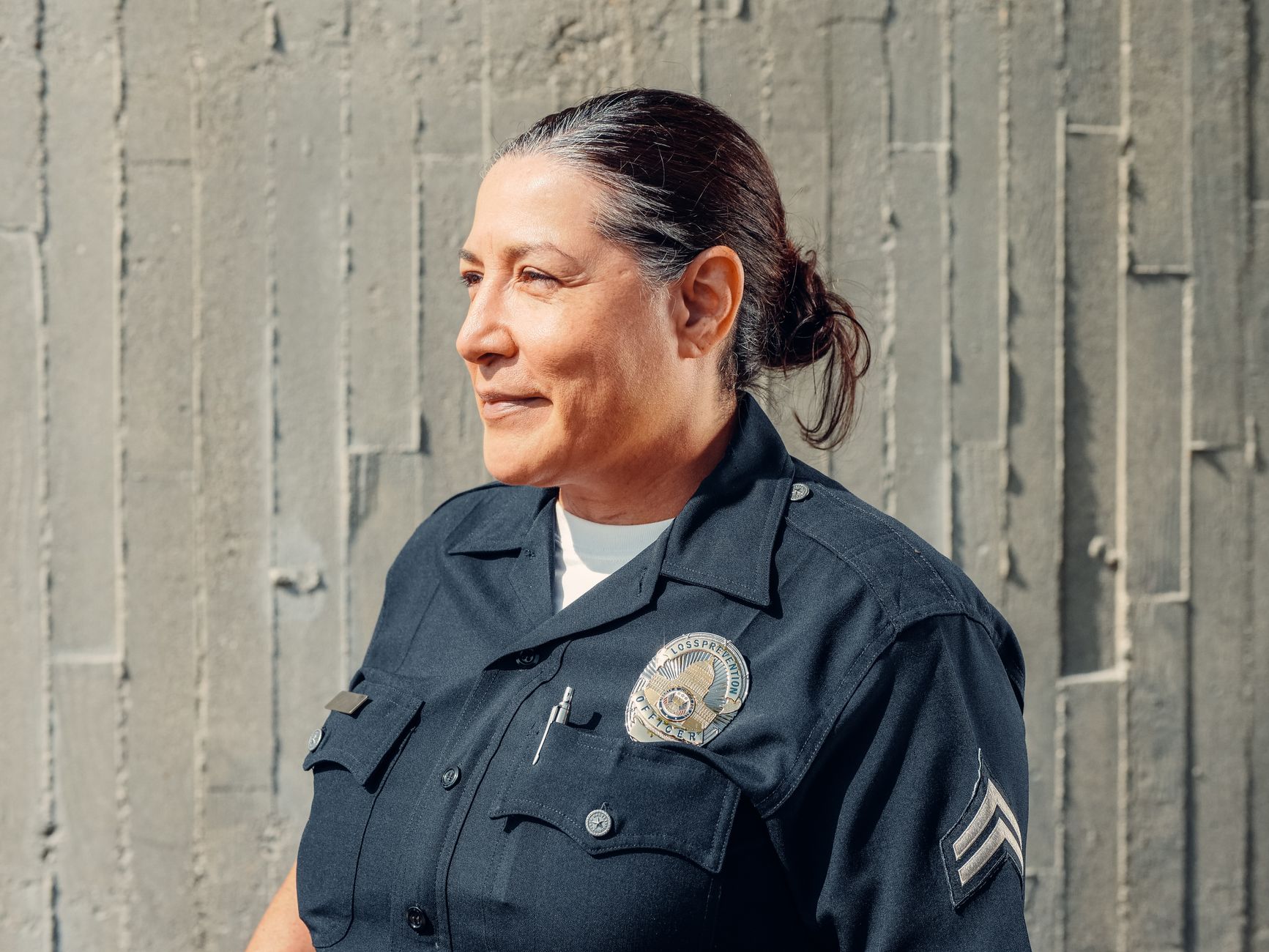 Portrait of a confident female police officer in uniform, standing outdoors against a textured wall.