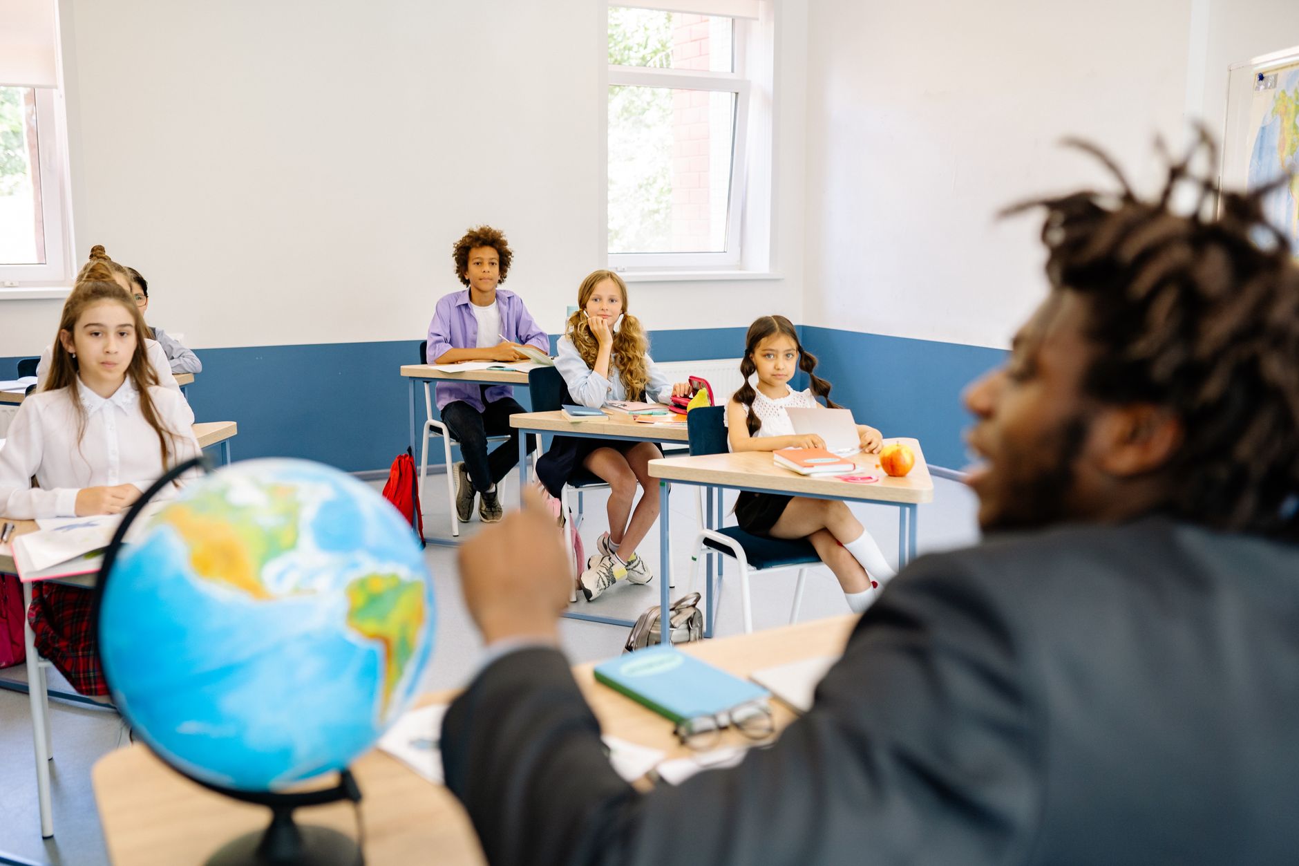 A diverse group of students and their teacher engaged in a classroom discussion with a globe on the table.