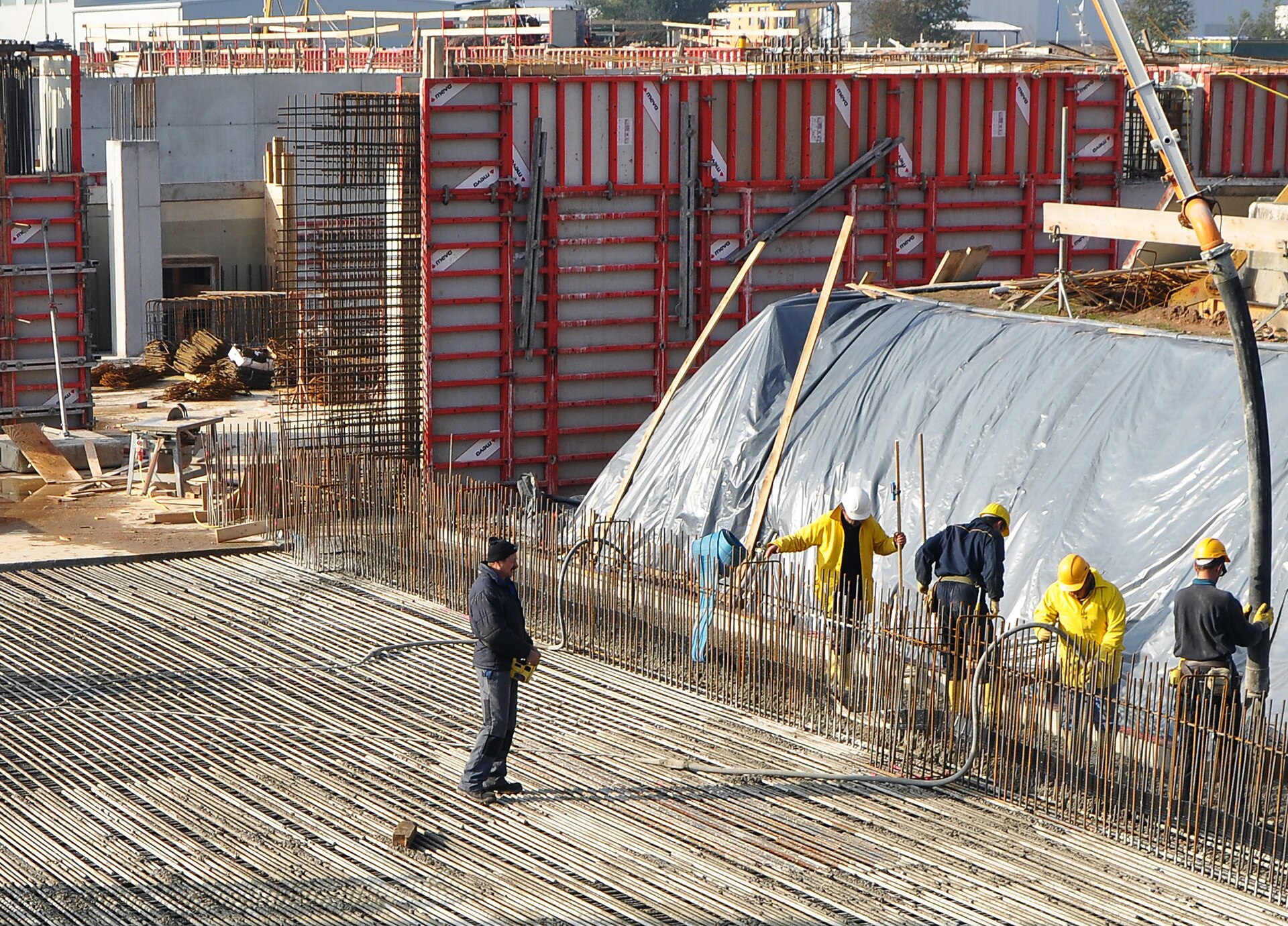 Betonierarbeiten auf der Baustelle. Vorne: Einbringen des Betons, Mitte: noch verschalter Beton, im Hintergrund: fertige Betonbauteile.