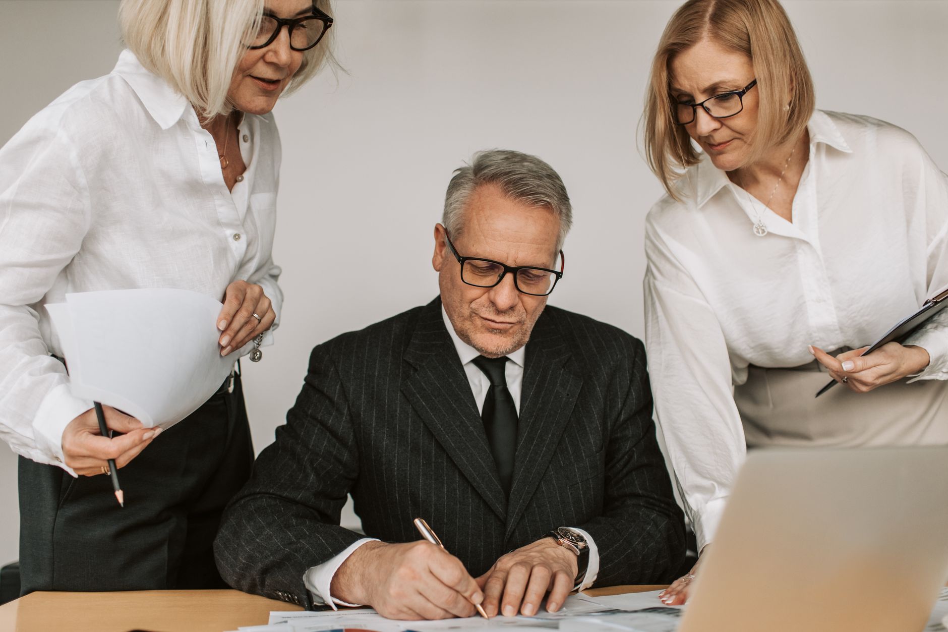 Senior professionals in an office setting reviewing and signing business documents together.