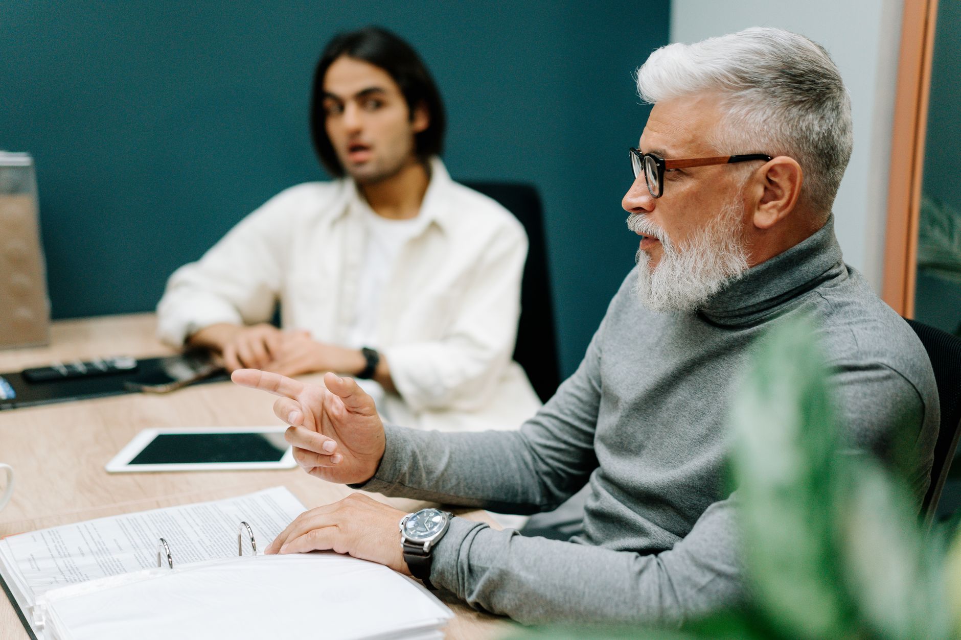 Senior professional gesturing while collaborating with colleague in a modern office.