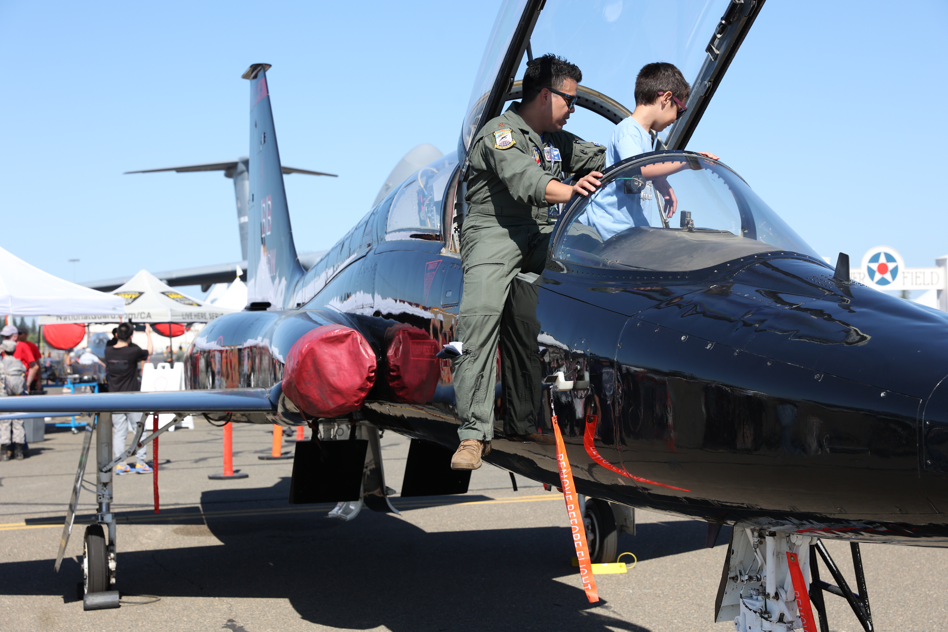 Pilot showing aircraft cockpit to a child at an airshow, emphasizing aviation and military education.
