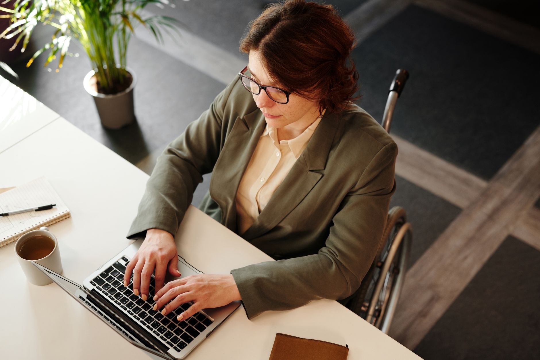 Professional woman in a wheelchair working on a laptop at an office desk.