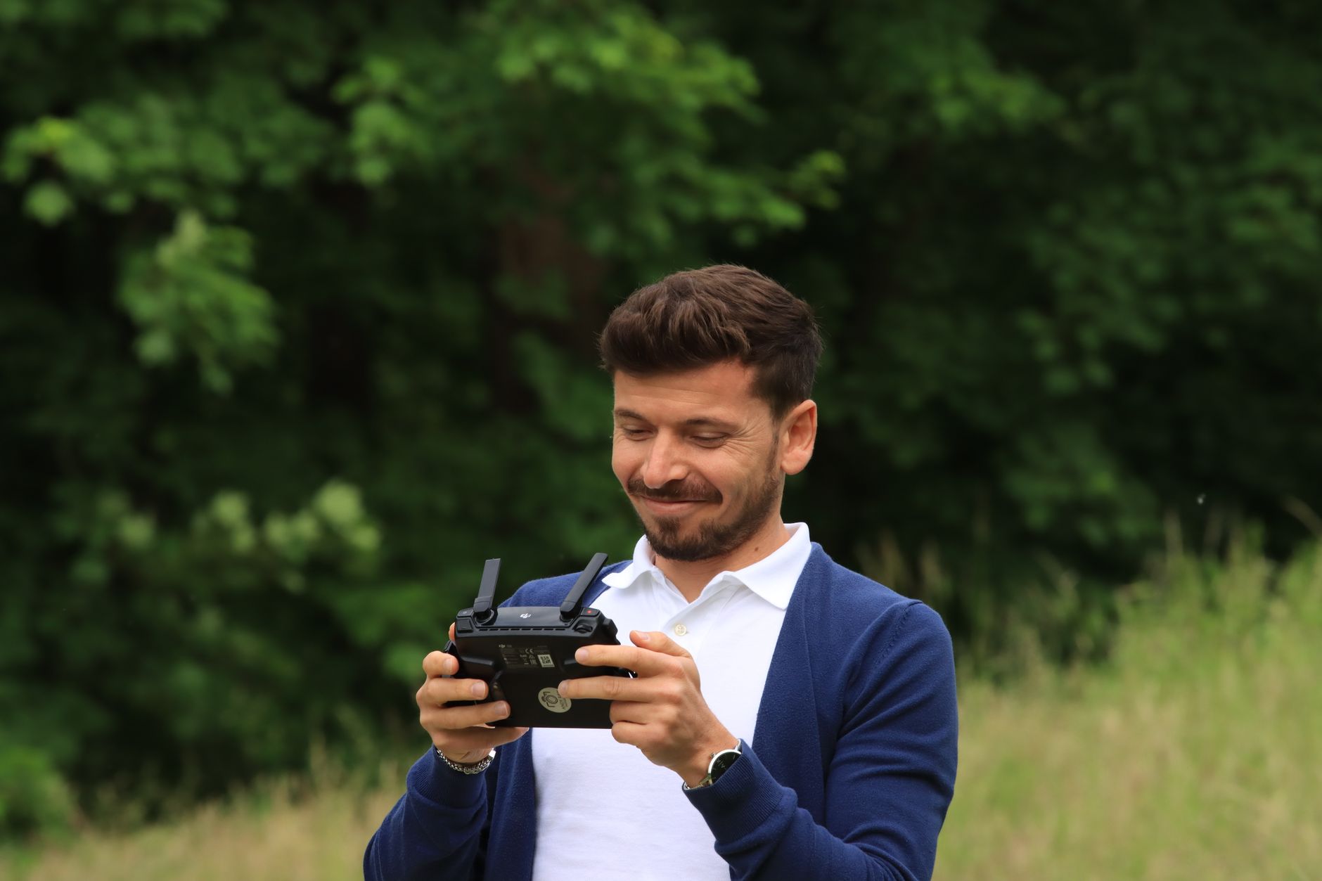 Smiling man using drone controller outdoors in a lush green setting.
