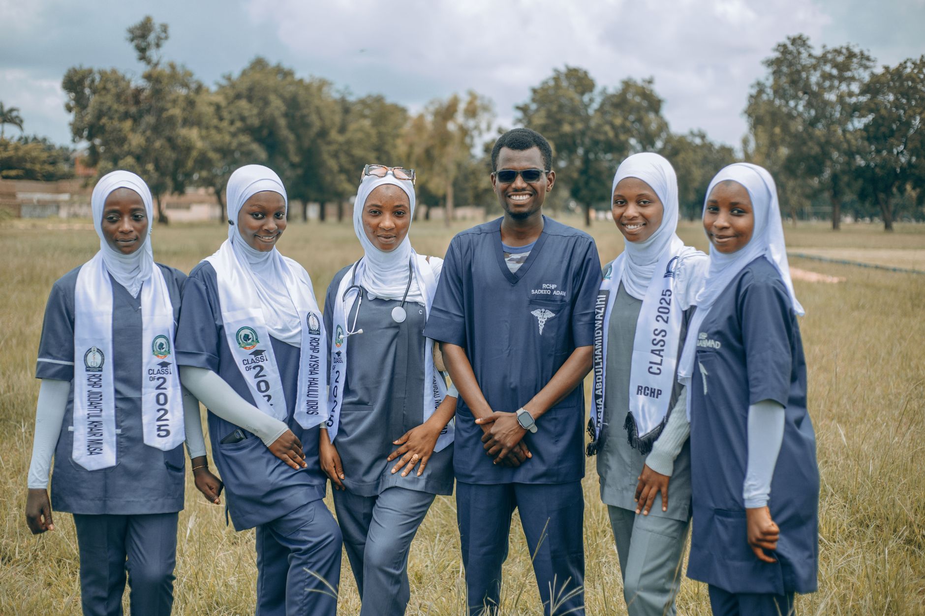 A group of smiling medical students in uniforms posing outdoors, showcasing diversity and teamwork.