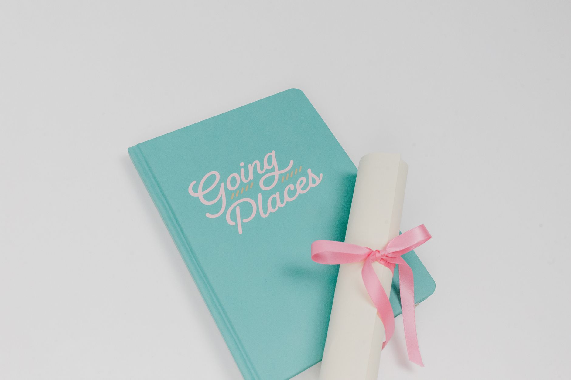 Teal notebook labeled 'Going Places' with a diploma wrapped in pink ribbon on a white surface.