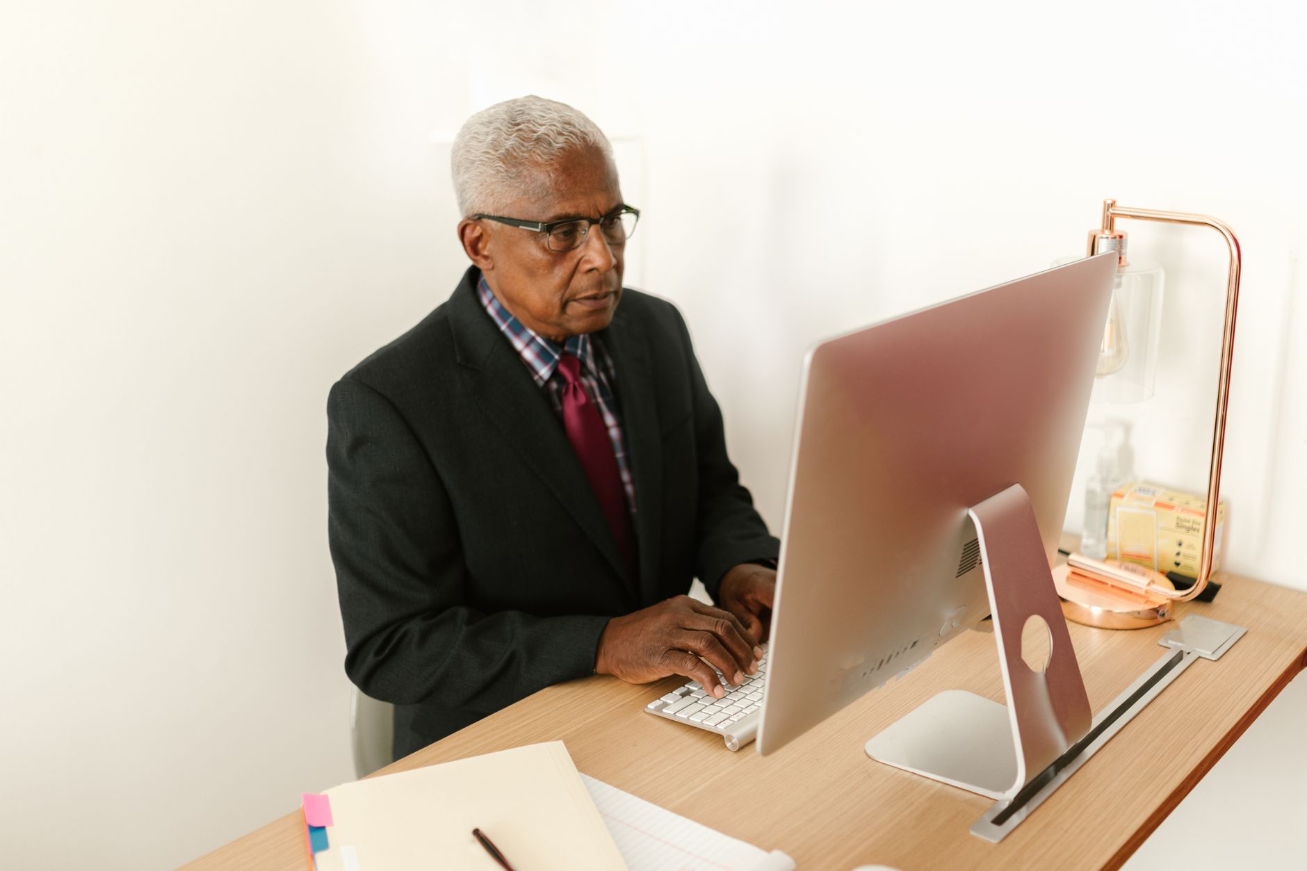 Senior man in corporate attire focusing on work at his desktop computer in a modern office.