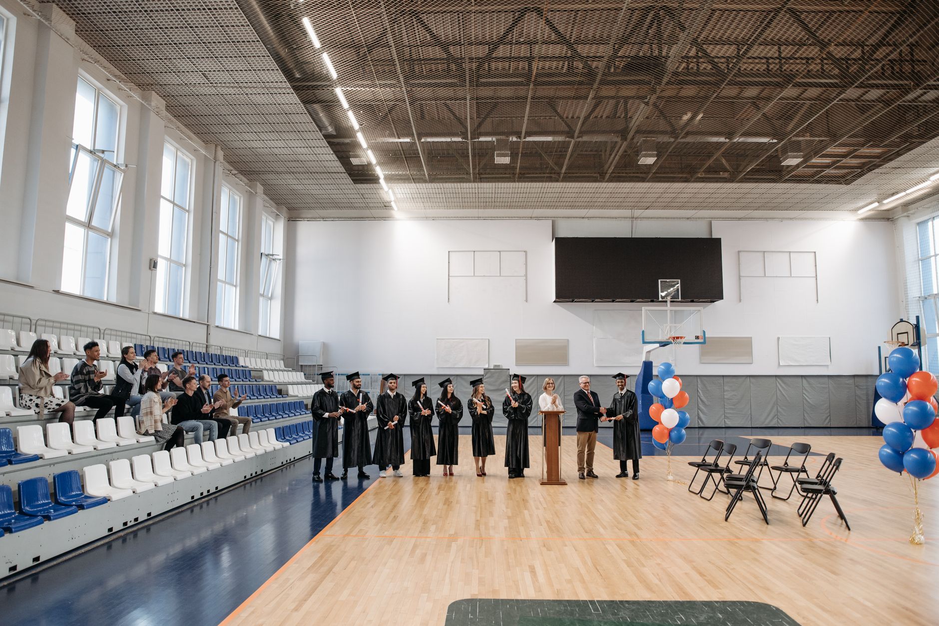 A graduation ceremony held in an indoor gymnasium with graduates and an audience.