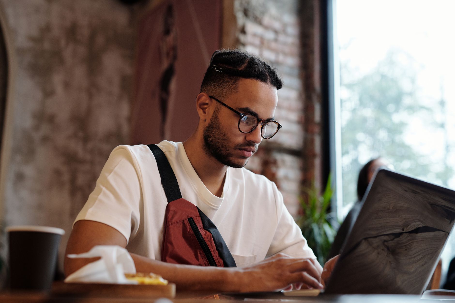 Young adult male freelancer working intently on a laptop in a cozy cafe setting.