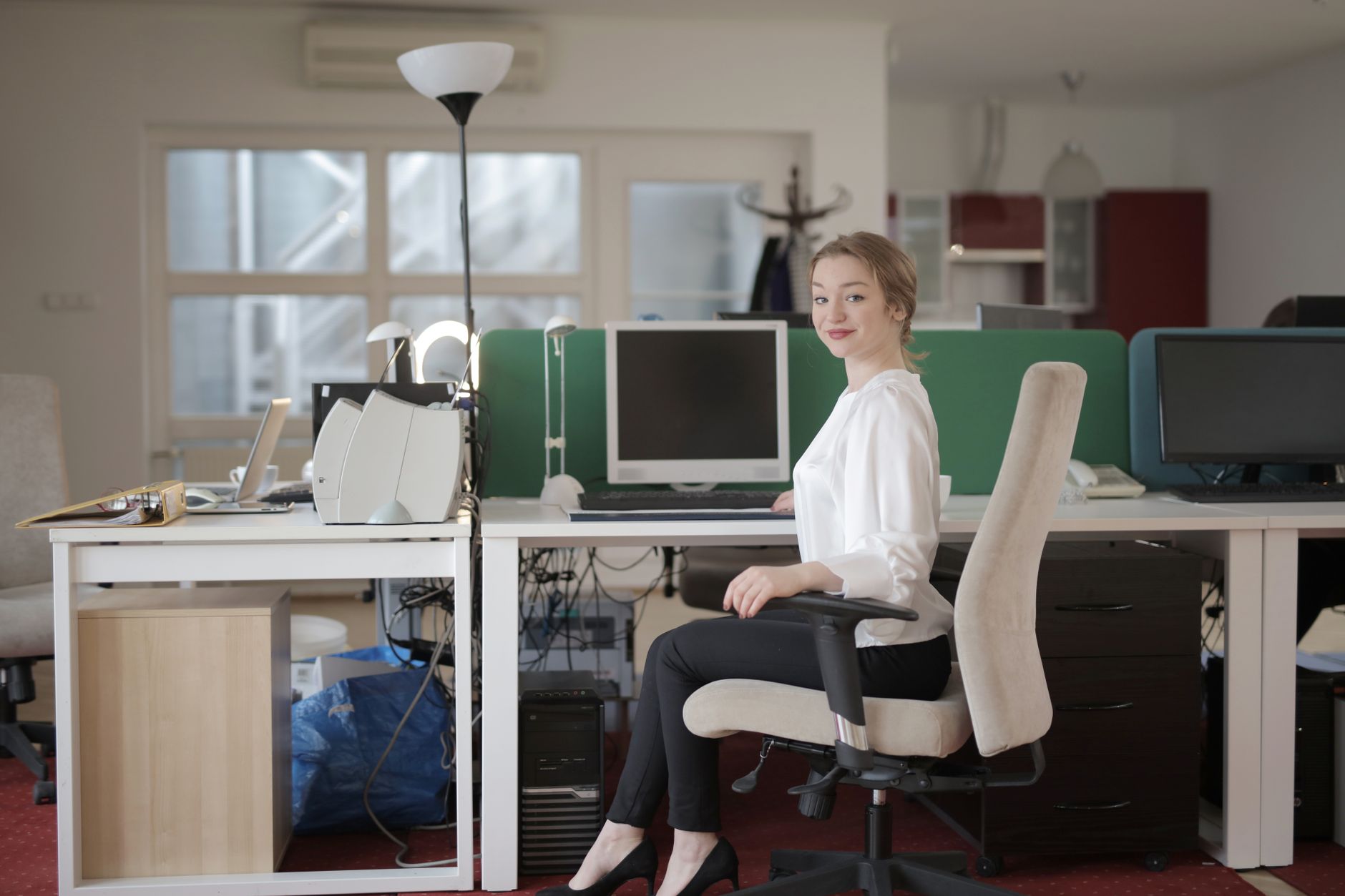 Side view of glad female worker in classy outfit sitting at table on office chair during work in modern workplace and looking at camera