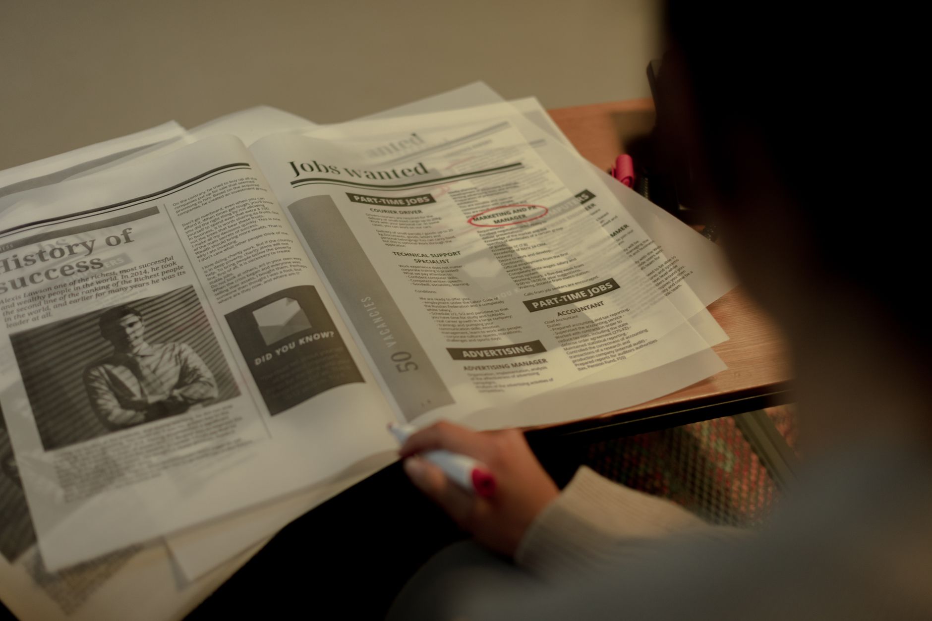 Person reviewing job listings in a newspaper, holding a pink marker for highlighting job ads.
